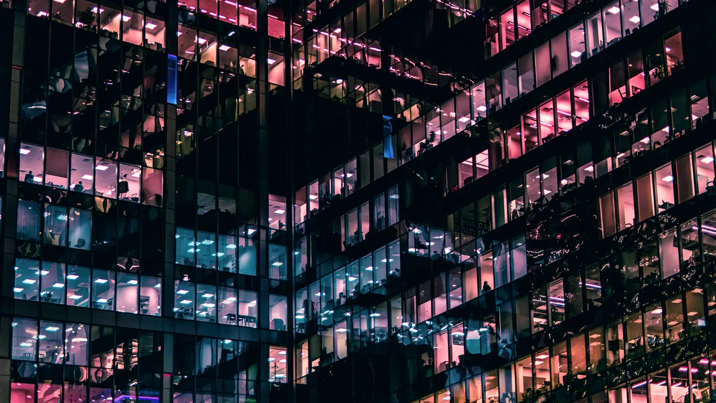 Office building at night with lit floors behind glass walls