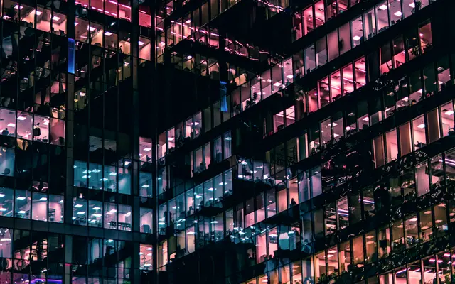 Office building at night with lit floors behind glass walls