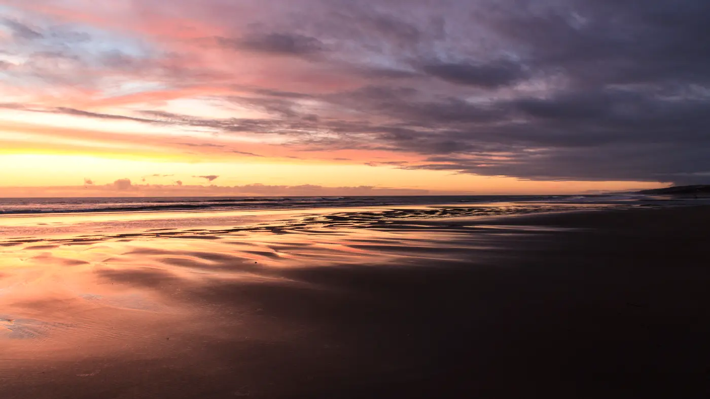 Calm beach at dusk under pink and purple clouds