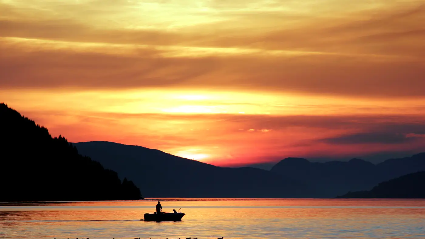 Small fishing boat on a mountain lake at golden sunset