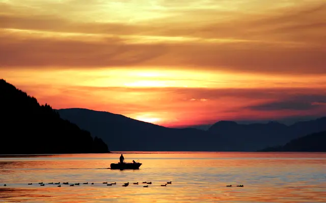 Small fishing boat on a mountain lake at golden sunset