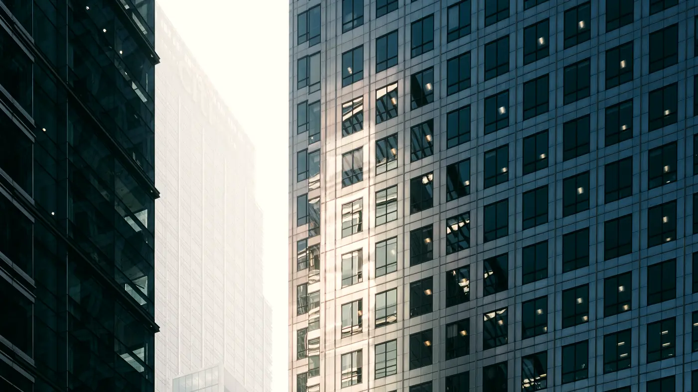 Blue glass office facade beside a tower in morning haze
