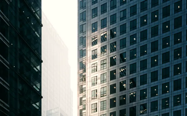 Blue glass office facade beside a tower in morning haze