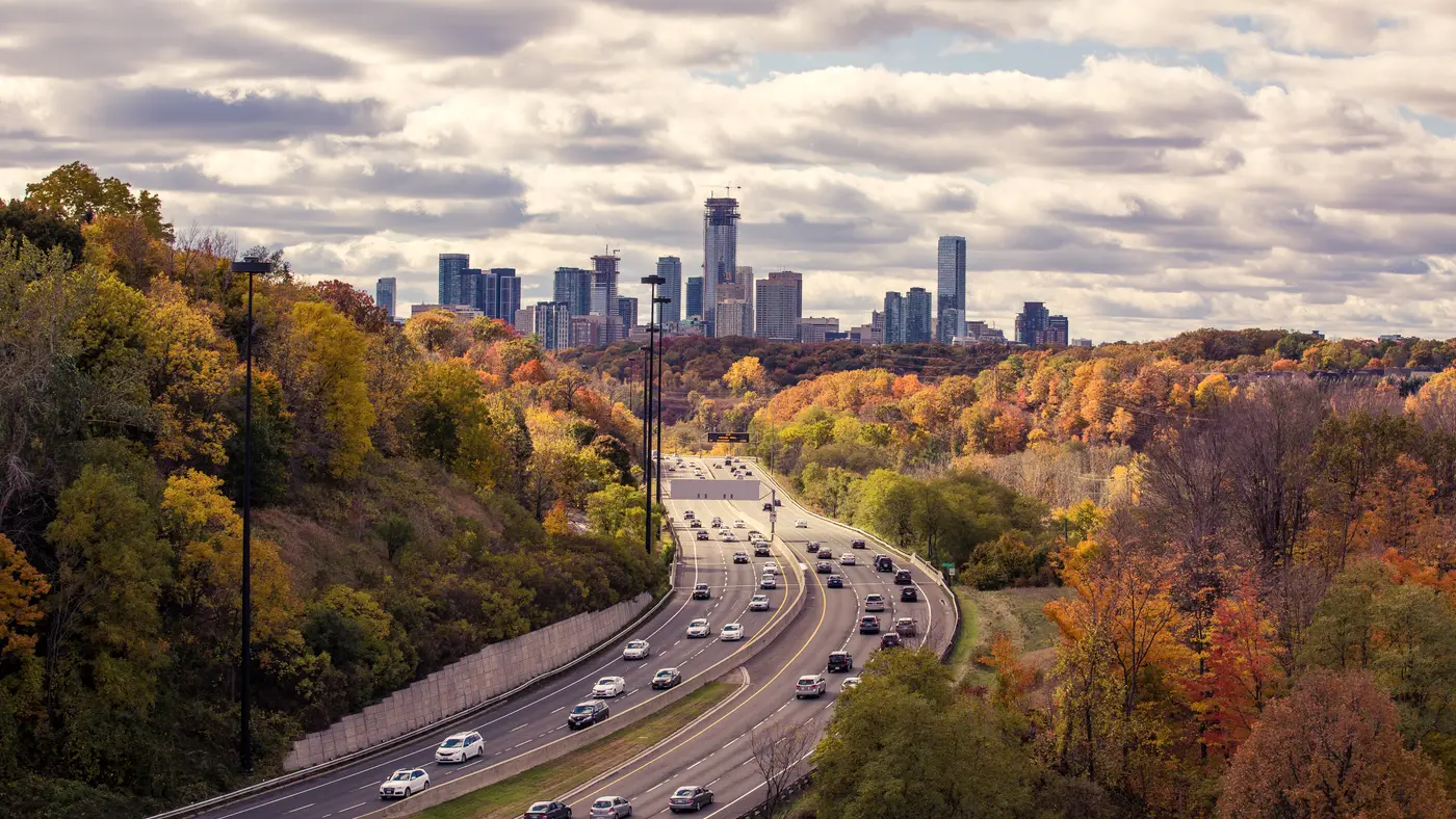 Highway through autumn trees leading toward a distant skyline
