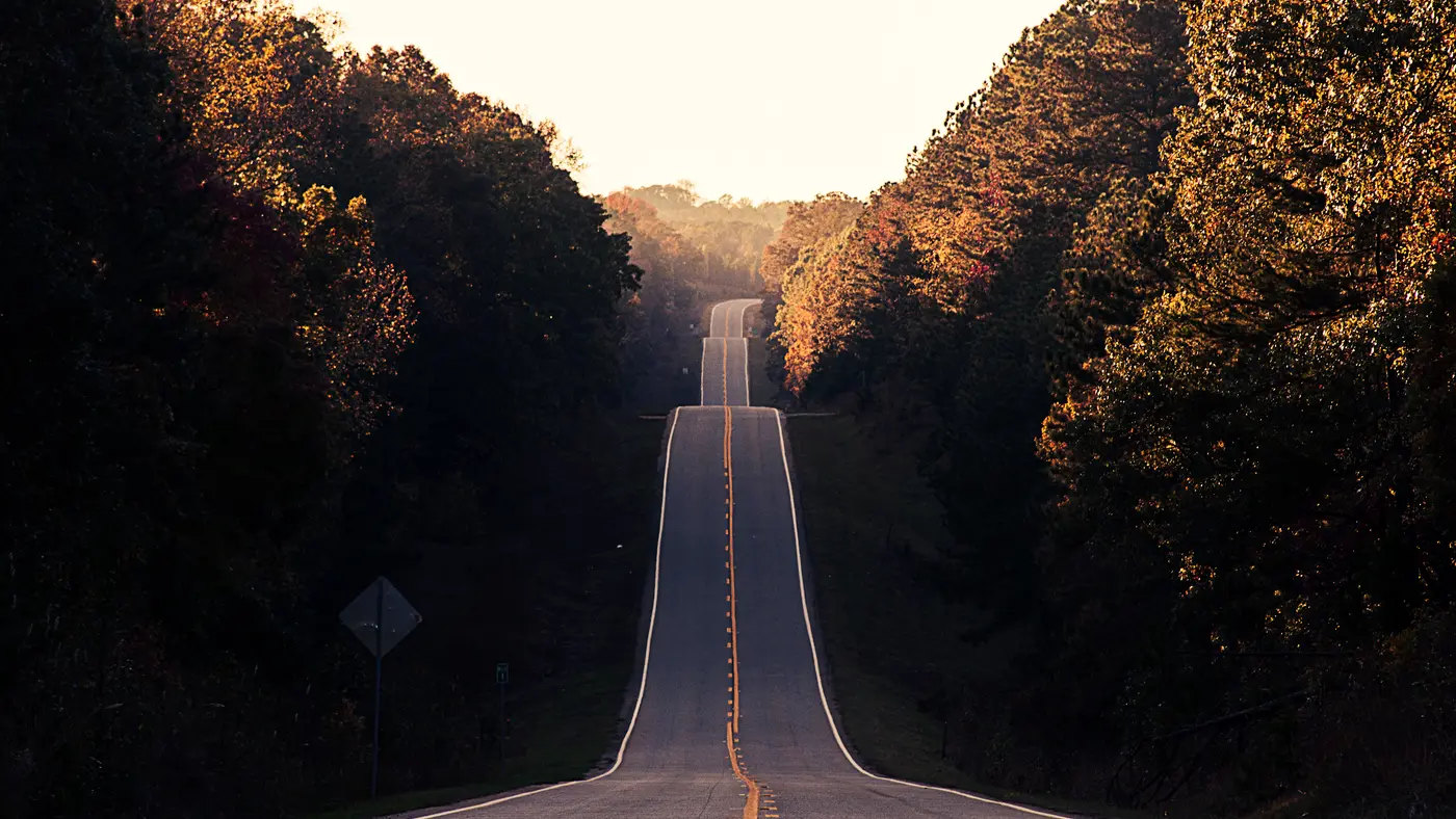 Straight road rising over hills between dark forest