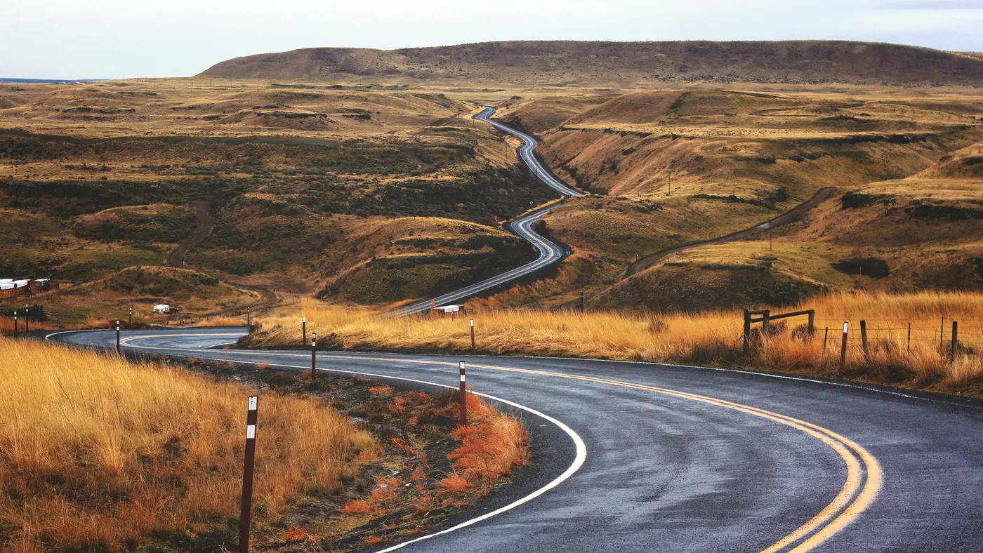 Winding road snaking through golden grassland hills