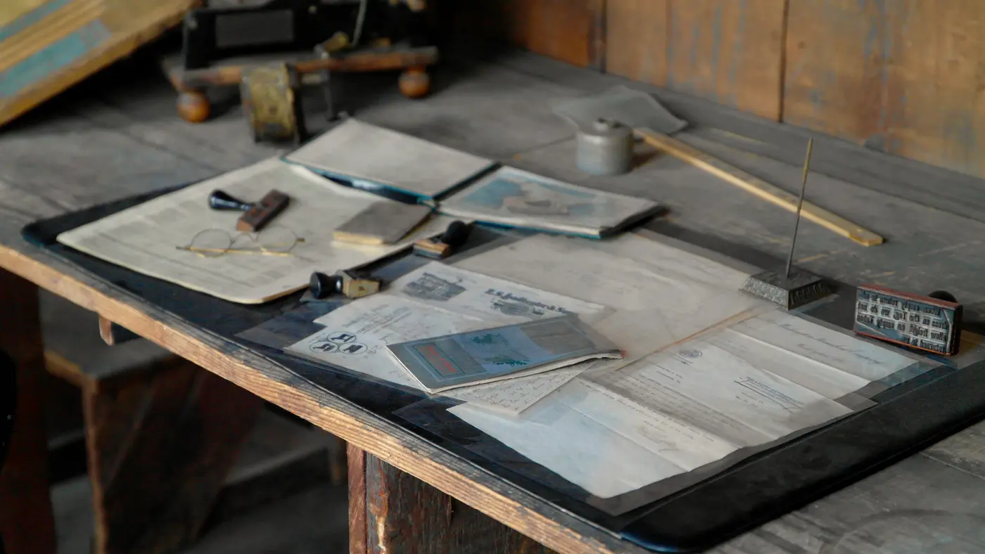 Old wooden desk covered with papers, notebooks and a pen