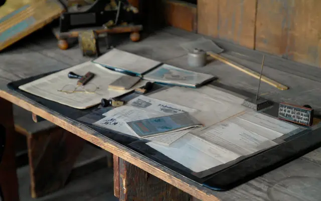Old wooden desk covered with papers, notebooks and a pen