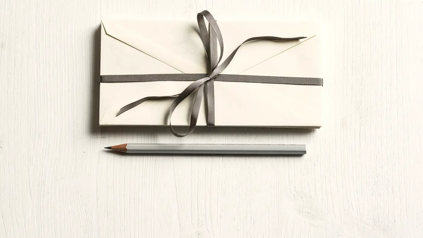 White envelopes tied with grey ribbon beside a pencil