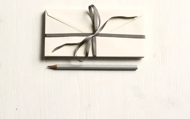 White envelopes tied with grey ribbon beside a pencil