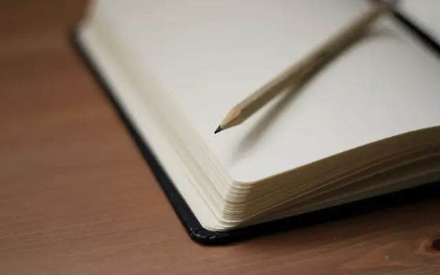 Open blank notebook with a pencil on a wooden table