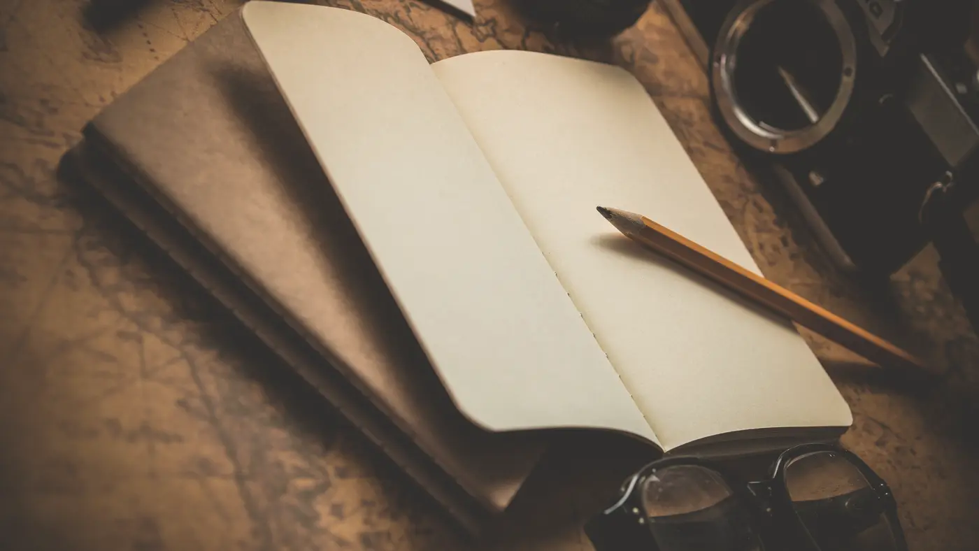 Open notebook with a pencil and glasses on a wooden desk