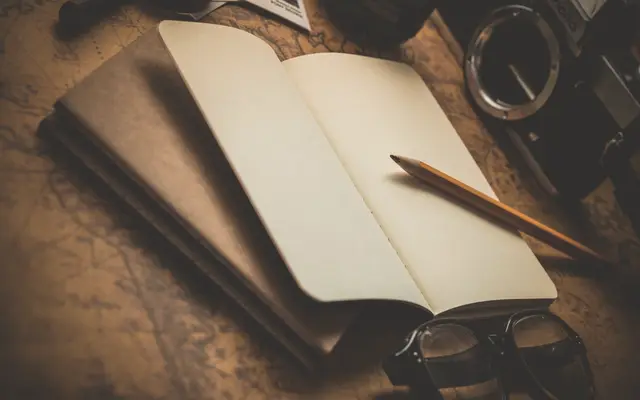 Open notebook with a pencil and glasses on a wooden desk