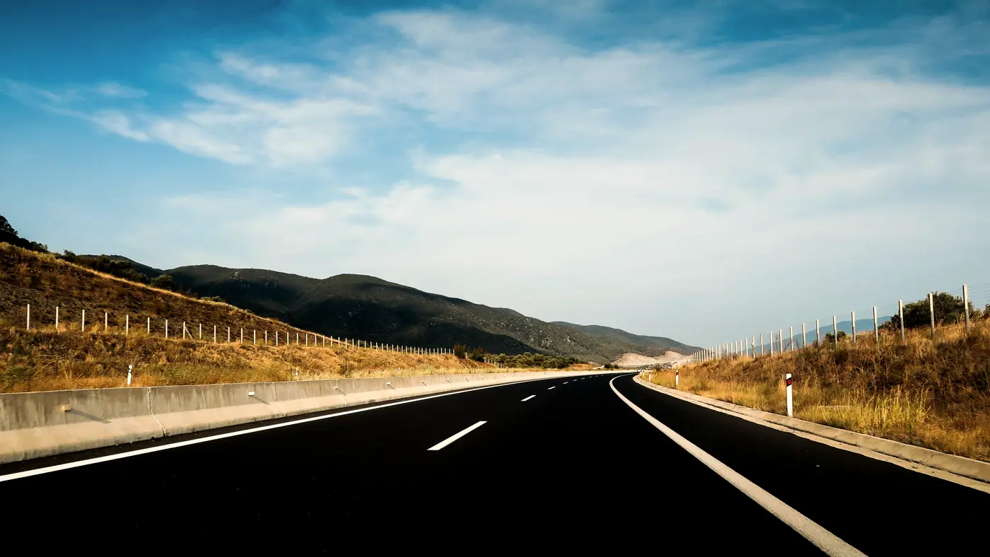 Open highway through dry hills under a wide blue sky
