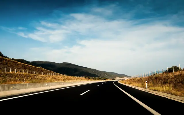 Open highway through dry hills under a wide blue sky