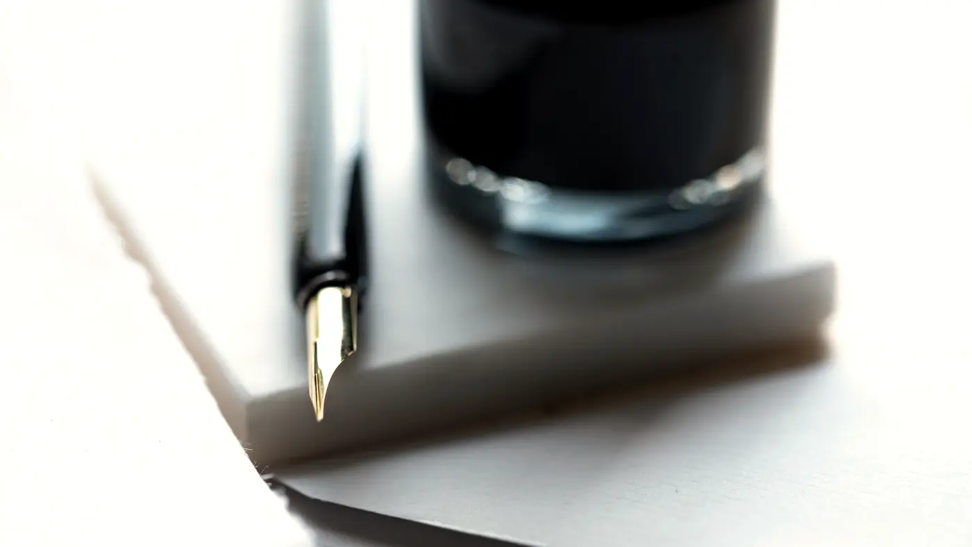 Fountain pen on stacked white paper beside an ink bottle