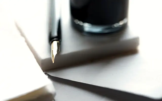 Fountain pen on stacked white paper beside an ink bottle