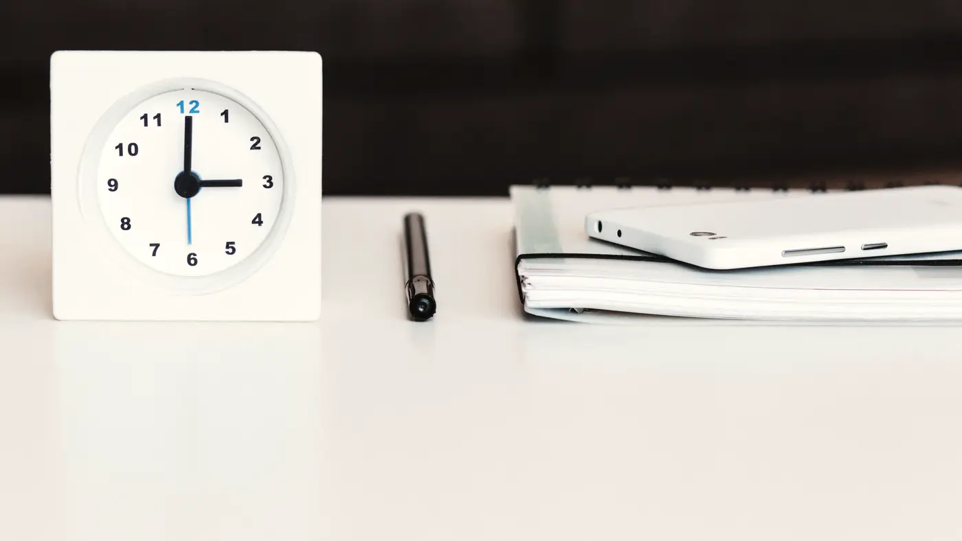White desk clock beside a pen and notebook