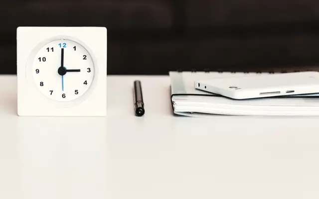 White desk clock beside a pen and notebook