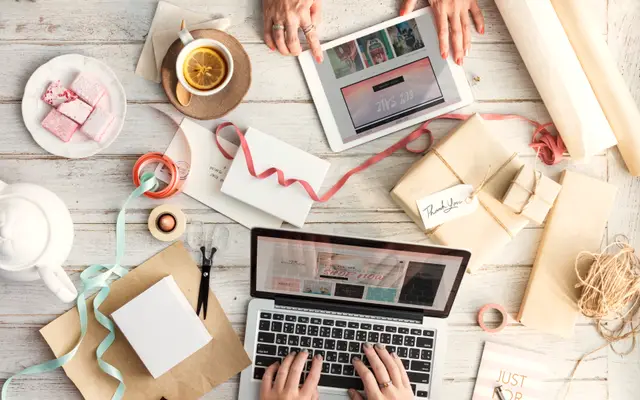 Hands typing on a laptop among gift boxes and wrapping