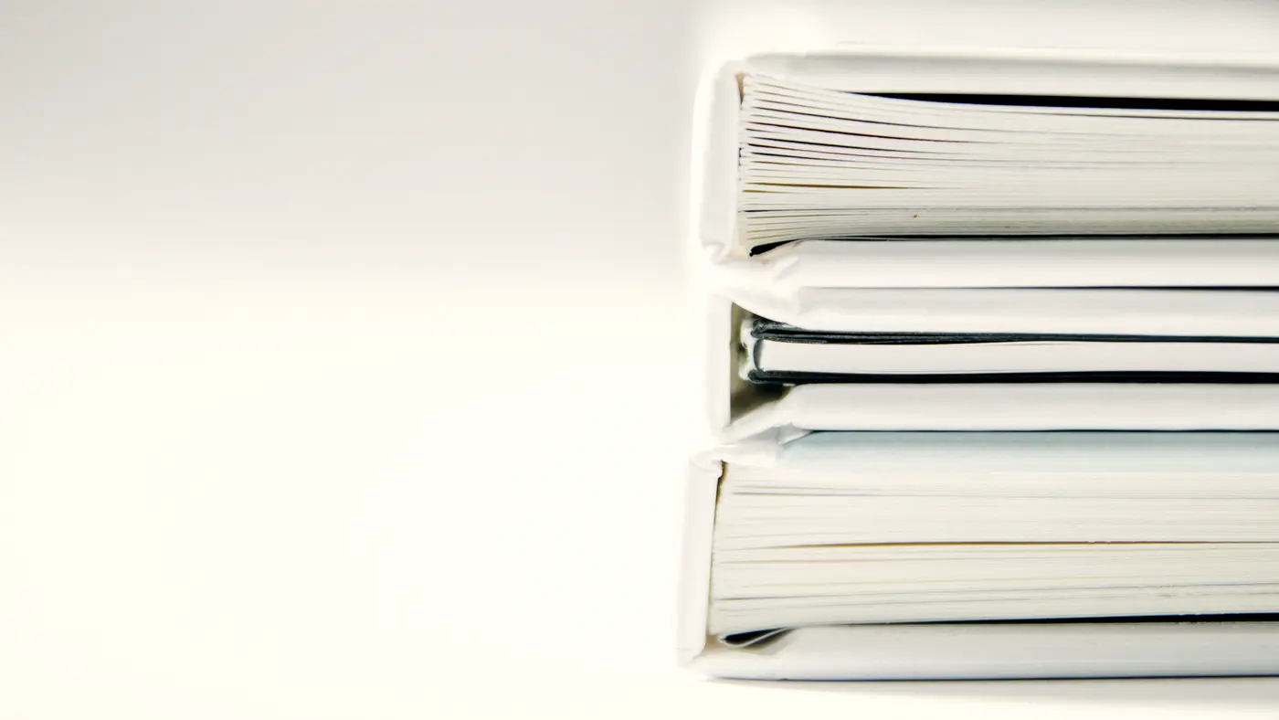 Stack of thick white ring binders on a white desk