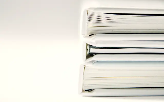 Stack of thick white ring binders on a white desk