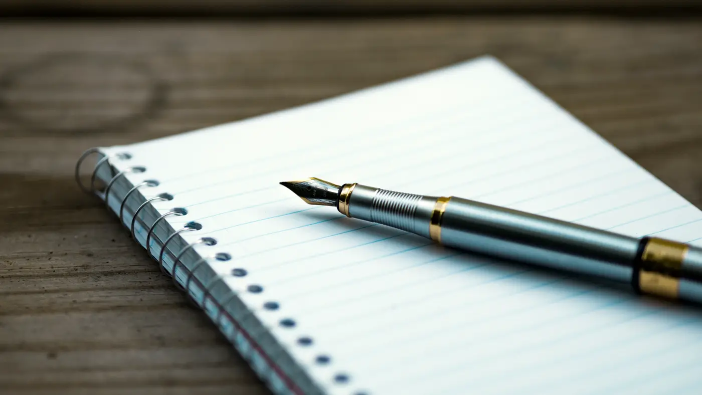 Fountain pen lying on a spiral notebook on a wooden table