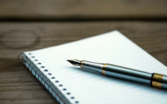 Fountain pen lying on a spiral notebook on a wooden table