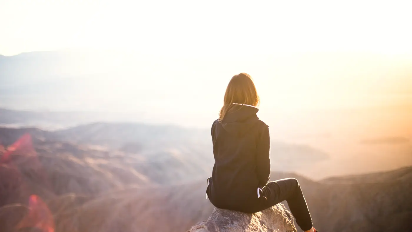Woman sitting on a rock overlooking hills at golden sunset