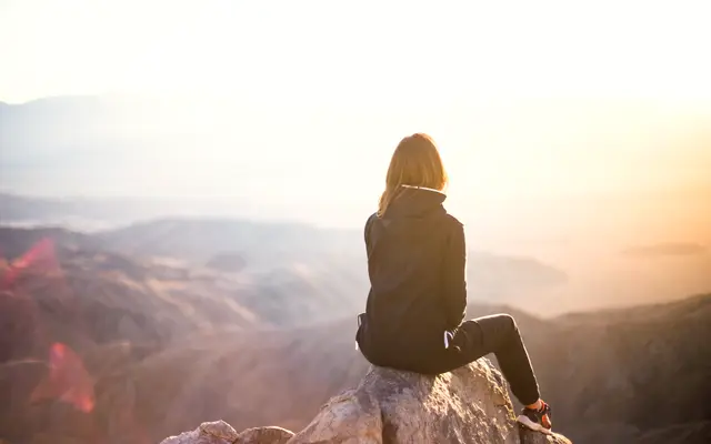 Woman sitting on a rock overlooking hills at golden sunset