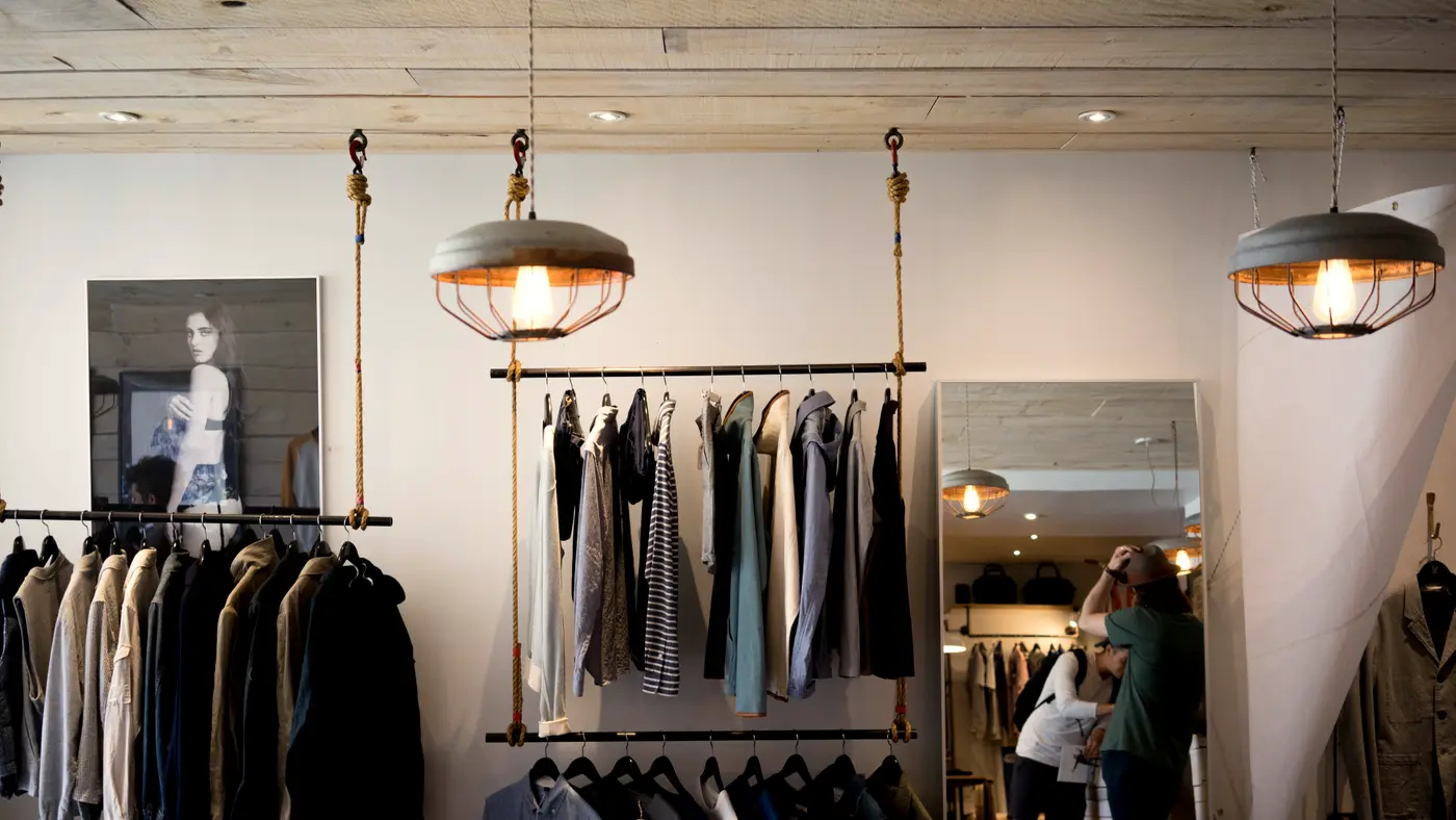 Bright independent clothing shop with pendant lamps and a customer