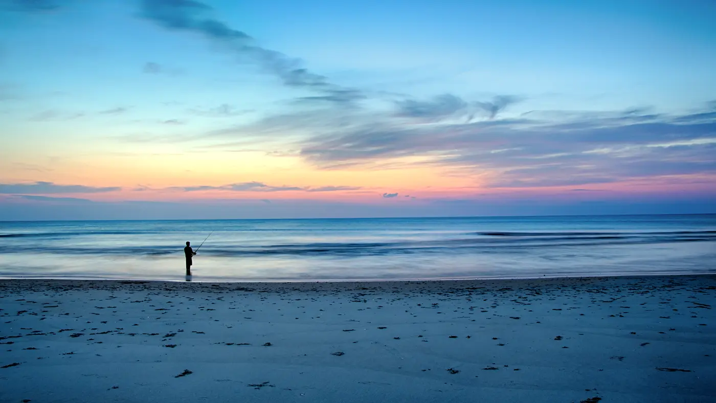 Lone angler fishing from a wide beach at blue hour