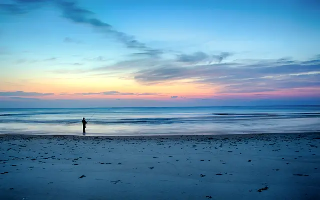 Lone angler fishing from a wide beach at blue hour