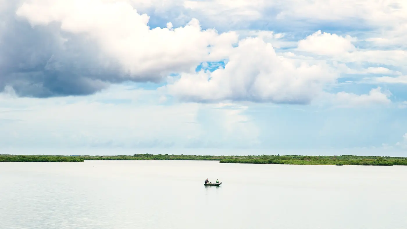 Small boat on a calm lake under a wide cloudy sky