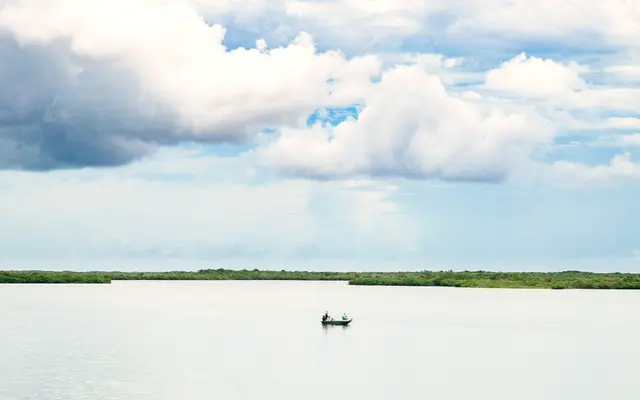 Small boat on a calm lake under a wide cloudy sky