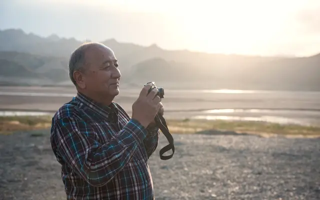 Older man holding a camera in soft evening light outdoors