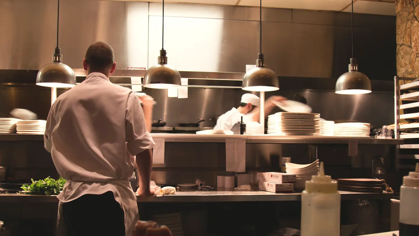 Cook working at the pass of a busy restaurant kitchen