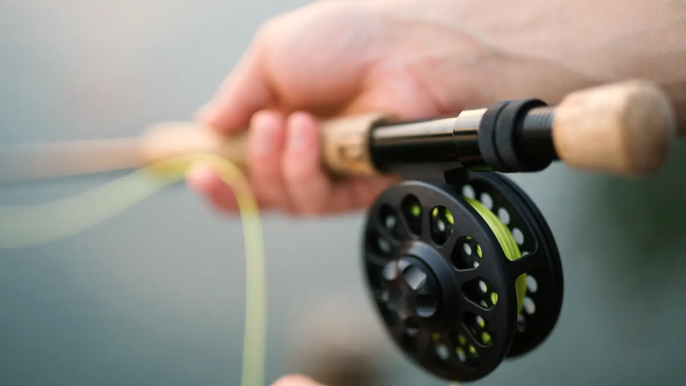 Hands holding a fly fishing rod and reel over water