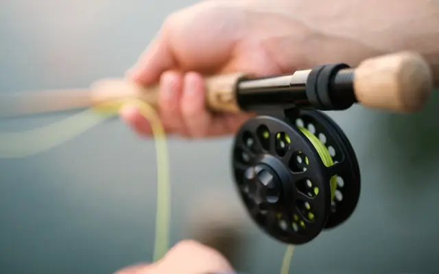 Hands holding a fly fishing rod and reel over water