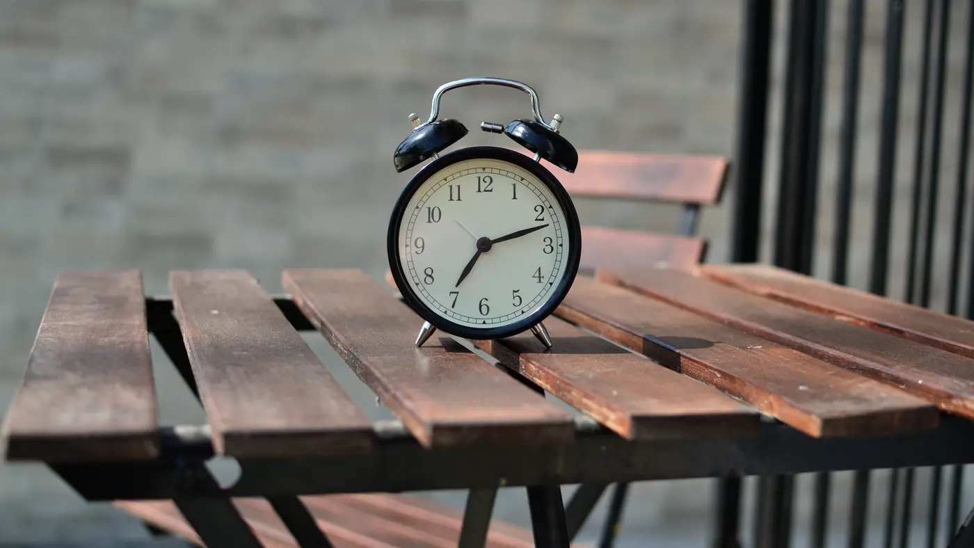Black alarm clock on a wooden slatted table outdoors