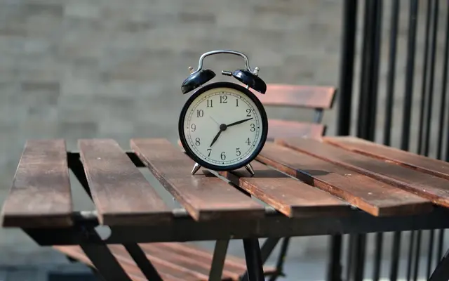 Black alarm clock on a wooden slatted table outdoors