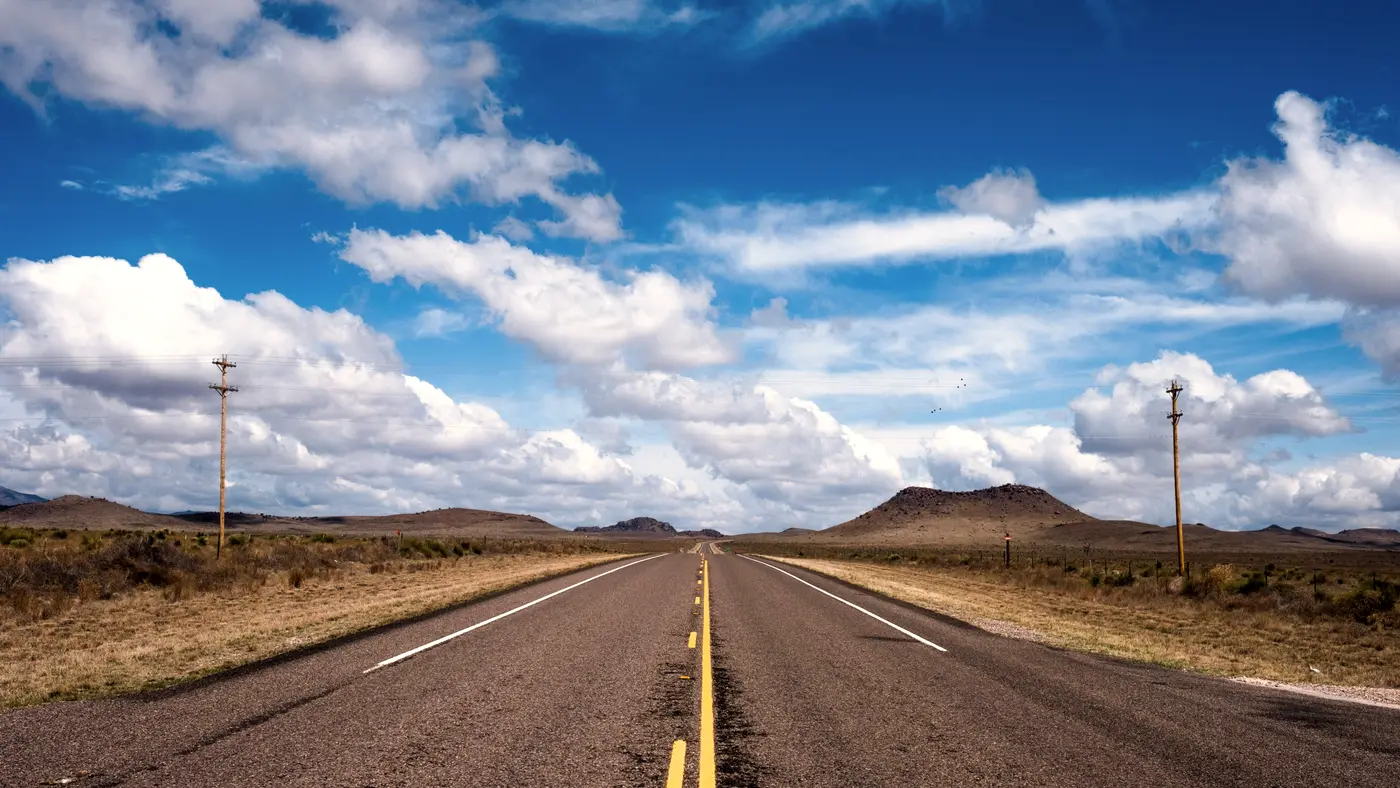Straight highway through open range under blue sky and clouds