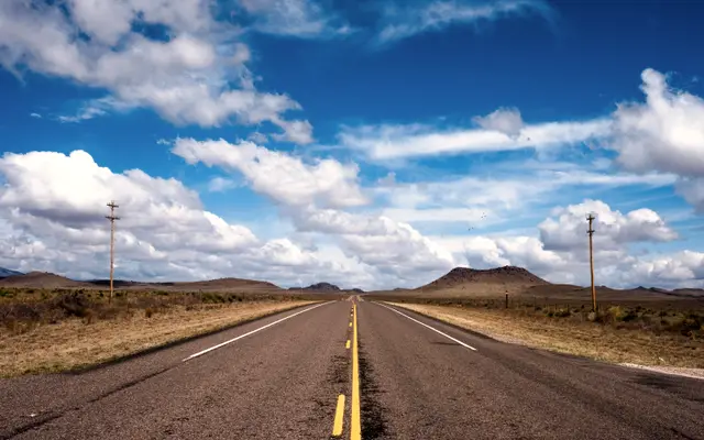 Straight highway through open range under blue sky and clouds