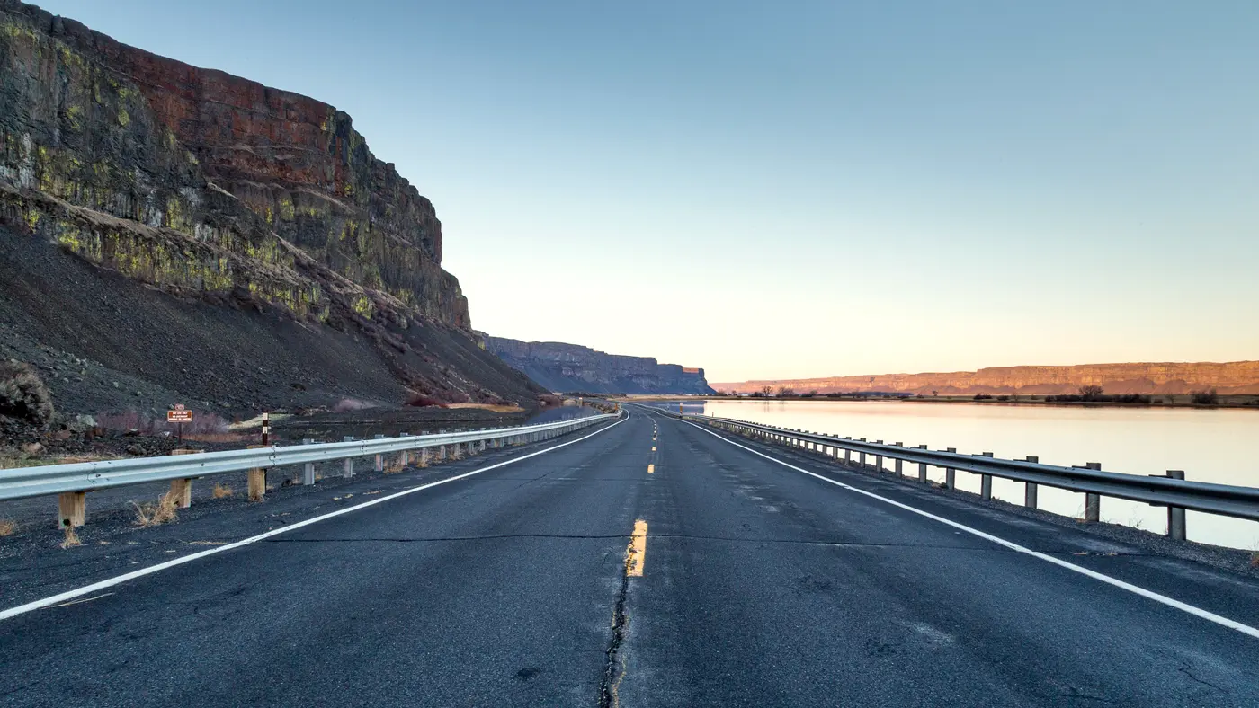 Empty highway running along a cliff and river at dawn
