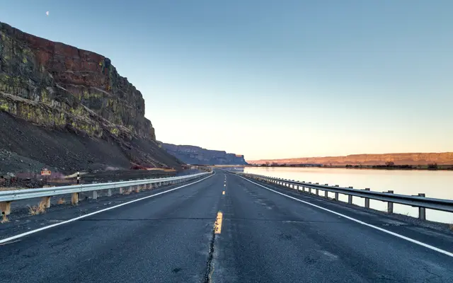 Empty highway running along a cliff and river at dawn