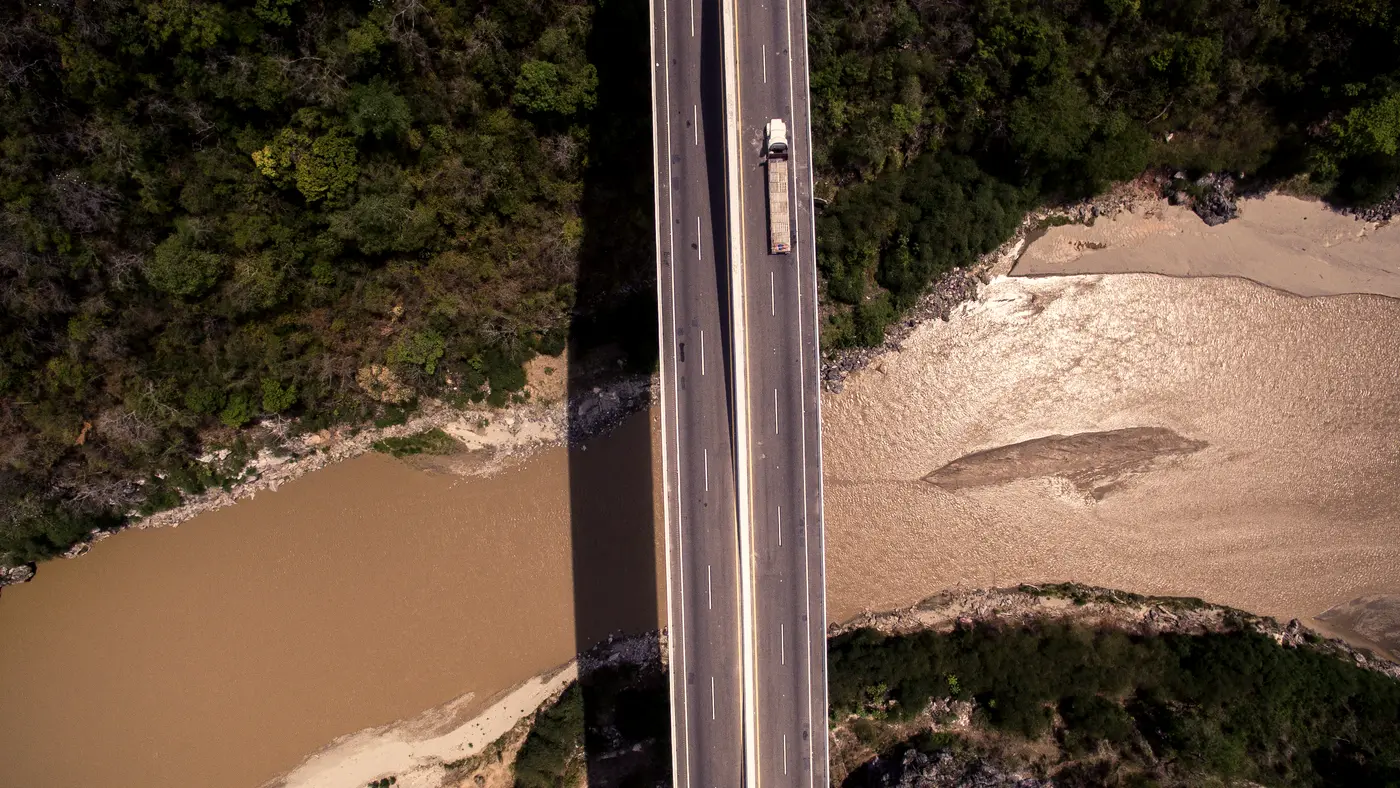 Aerial view of a straight road crossing forest and riverbank