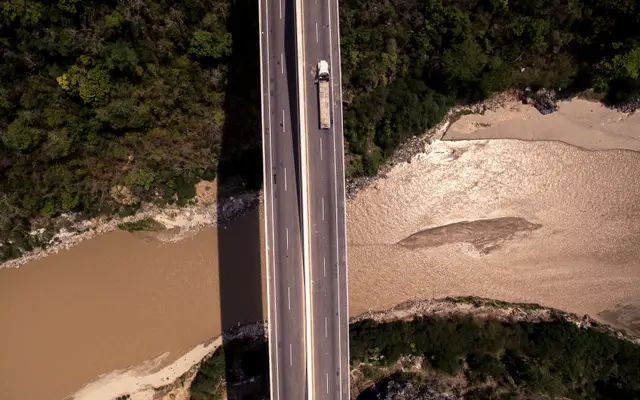 Aerial view of a straight road crossing forest and riverbank