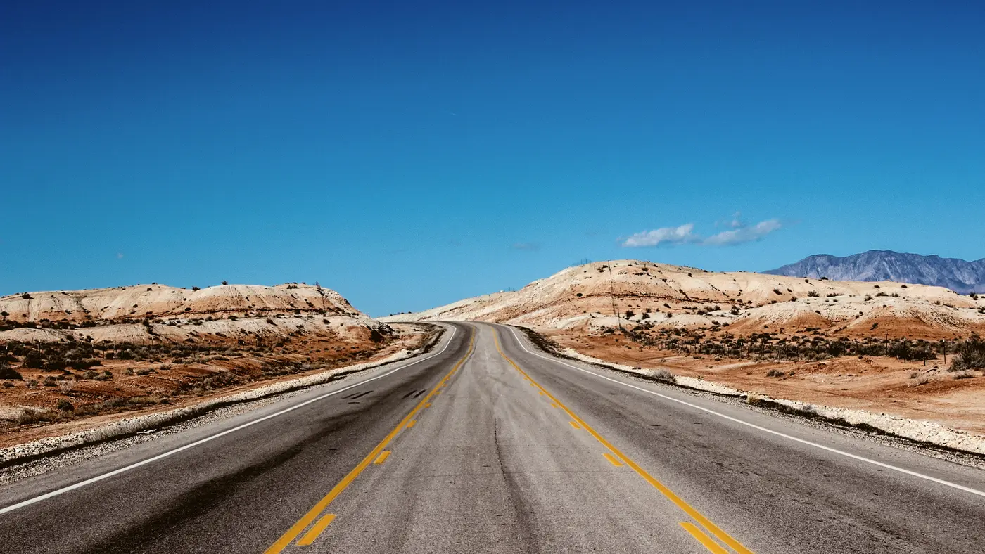 Open desert highway running between pale eroded hills
