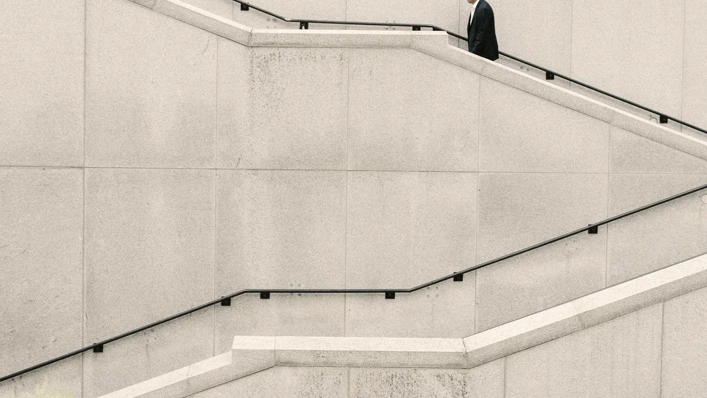 Businessman climbing a long concrete staircase along a pale wall
