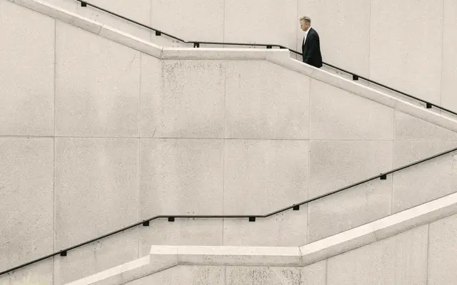 Businessman climbing a long concrete staircase along a pale wall